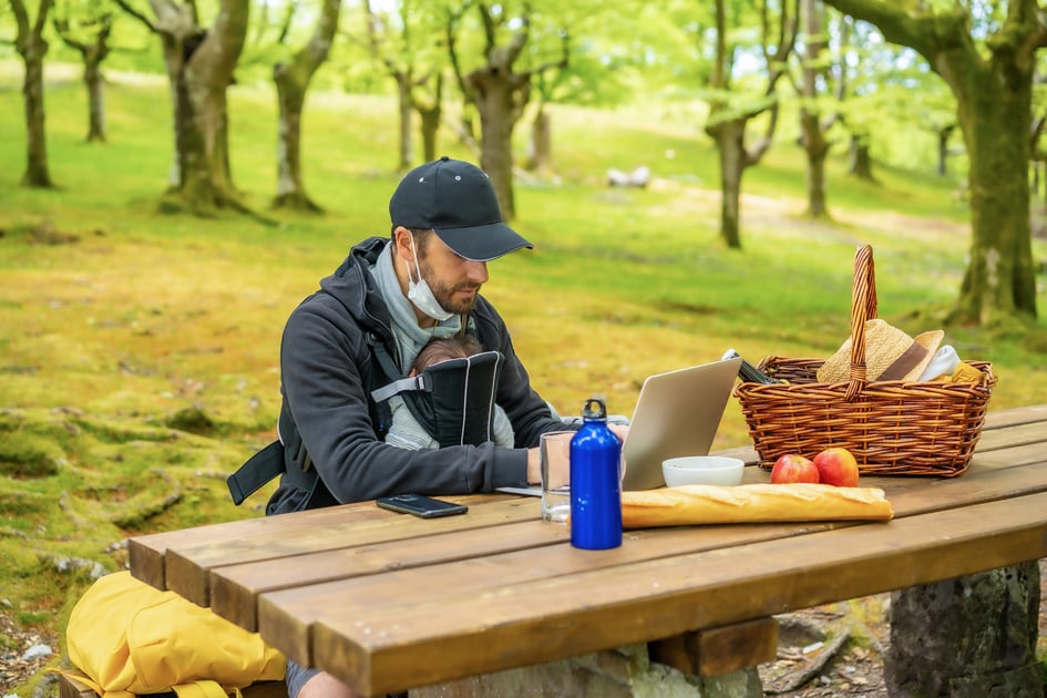 young-caucasian-father-teleworking-sitting-at-picnic-table-with-computer-in-the-woods